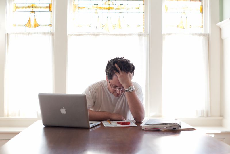 A man sits frustrated at a laptop computer.