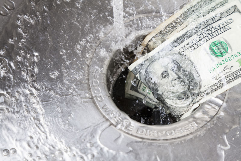 Money being washed down a garbage disposal.