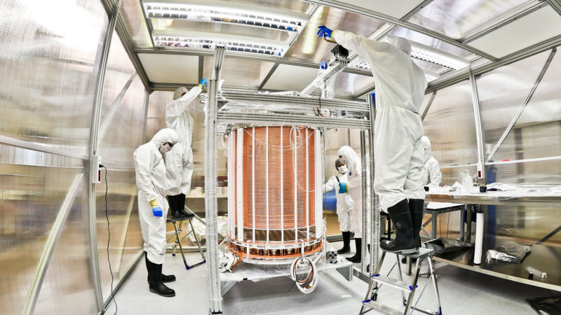 People in clean suits standing around a person-sized detector.