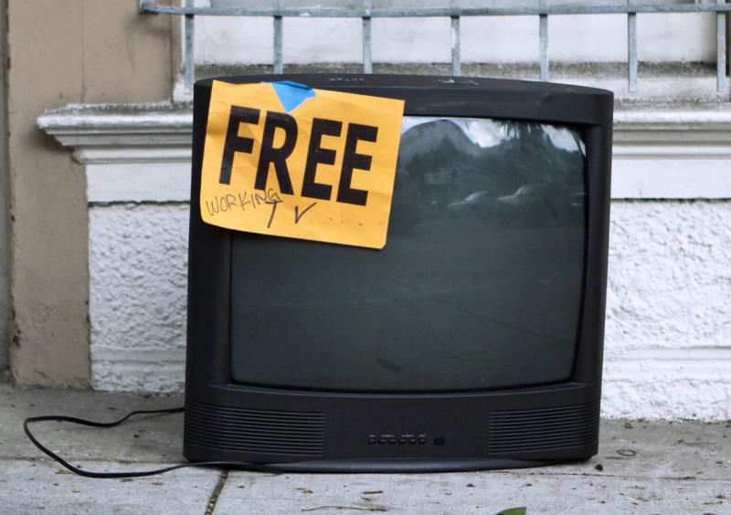 A TV set left on a sidewalk with a sign that says, 