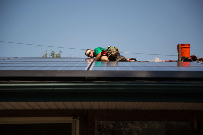 A man in construction gear assembles a solar panel on a residential roof.