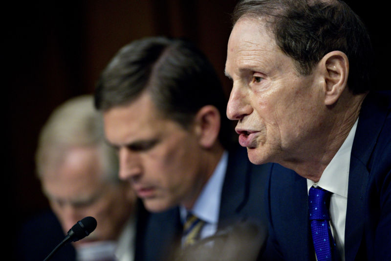 Men in suits talk into microphones.