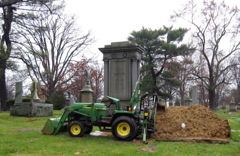 Stock photo of a gravedigging machine in front of a headstone.