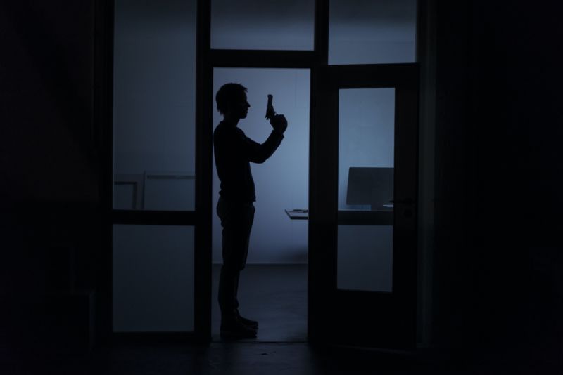 A man holding a gun, seen in a dark office.