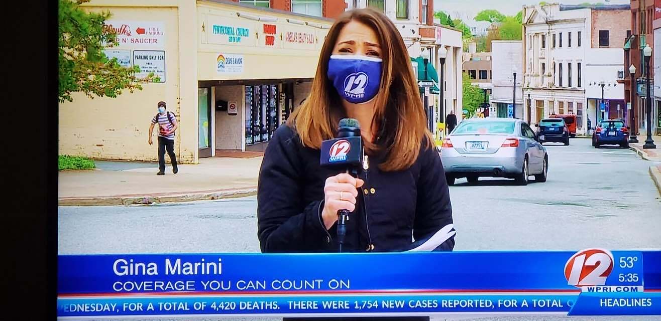 a female news anchor wearing a face mask and talking to a microphone