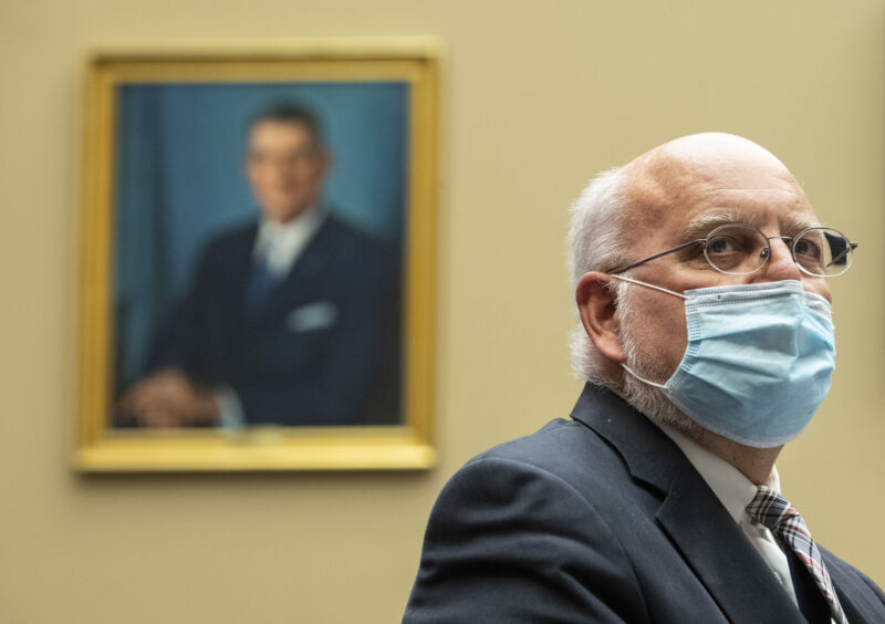 A serious man wears a suit and a face mask.