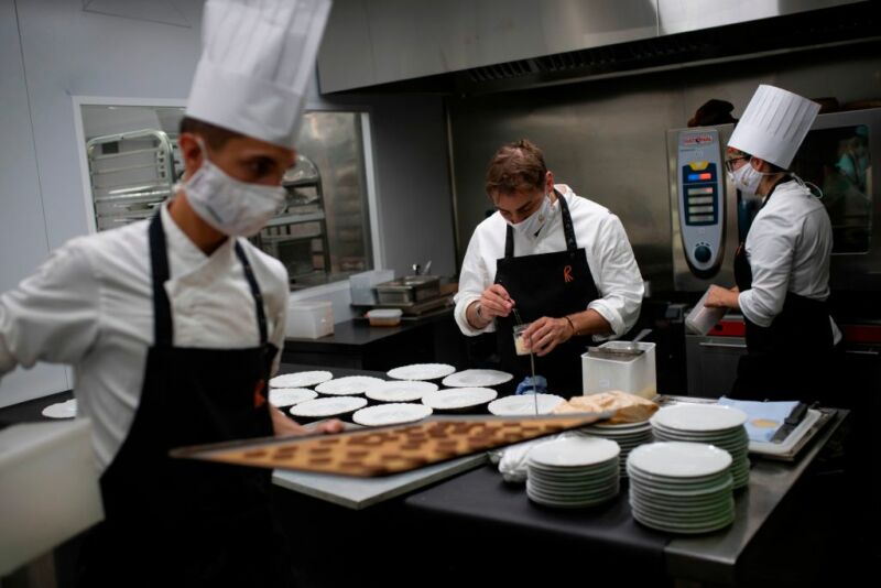 Masked chefs work in a professional kitchen.