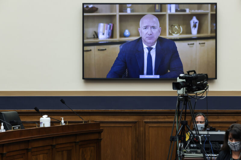 A man on a TV addresses a room of legislators.