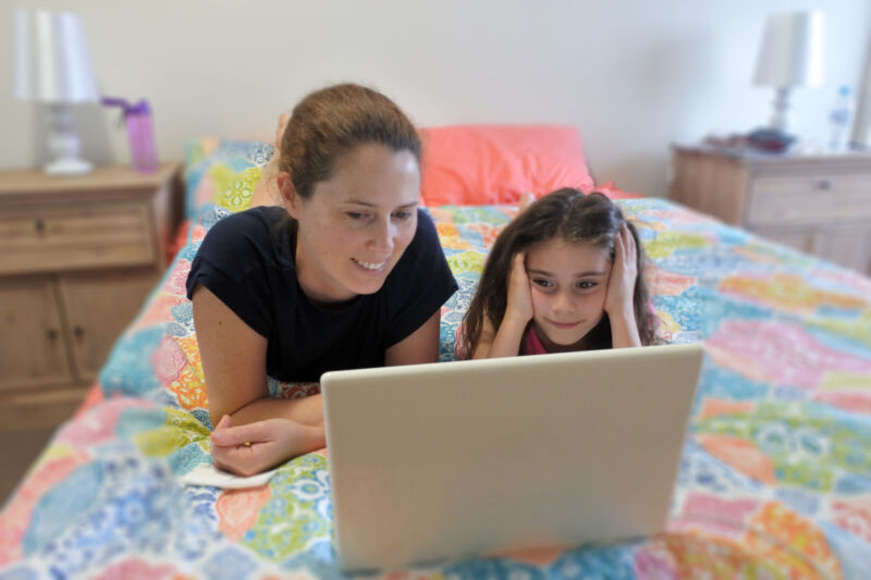 A mother and child daughter look at a laptop together.