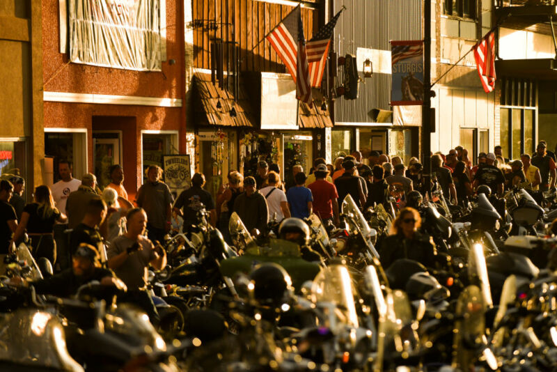 A small-town Main Street at night is cluttered with motorcycles and pedestrians.