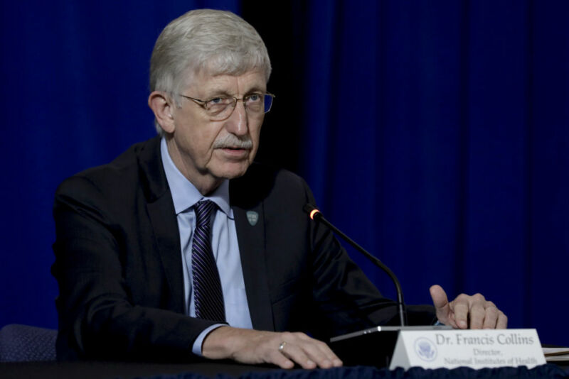 Image of an older male with glasses, seated at a microphone.