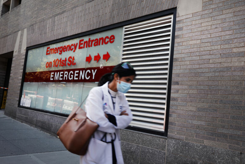 A doctor walks in front of a hospital entrance.