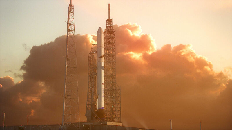 A rocket sits on a launch pad in front of a fiery sunrise.