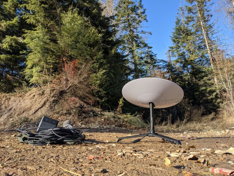 A SpaceX Starlink satellite dish placed on the ground in a forest clearing.