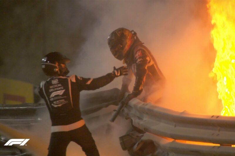 A racing driver is helped away from a fiery crash