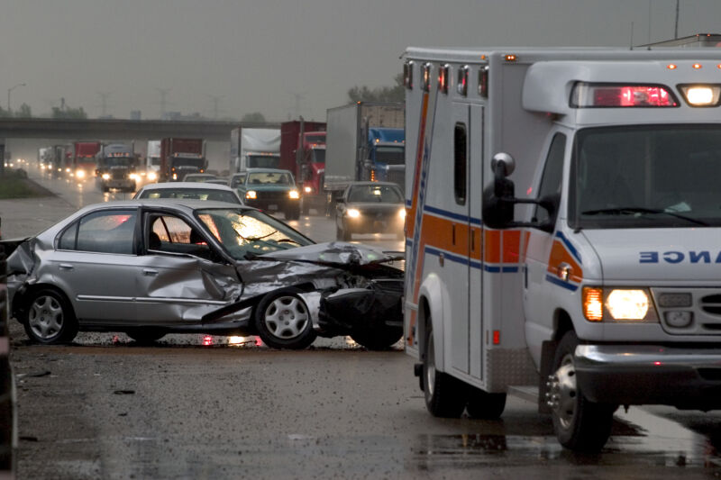 Car crash on major highway during rainfall at night. Ambulance in foreground and police car in background.