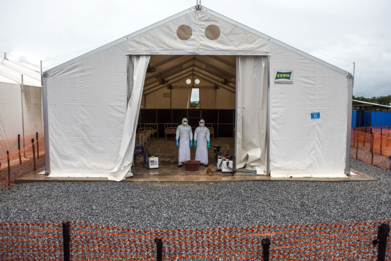 Health care workers wearing personal protective equipment stand in a tent with patient beds at an Ebola Treatment Center in Coyah, Guinea, on Thursday, Sept. 10, 2015.