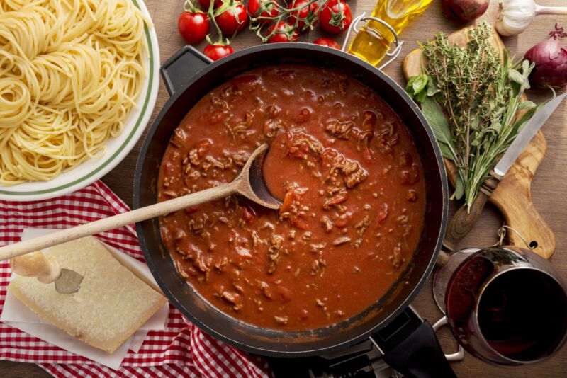 Bolognese sauce in a pan, next to a bowl of spaghetti.