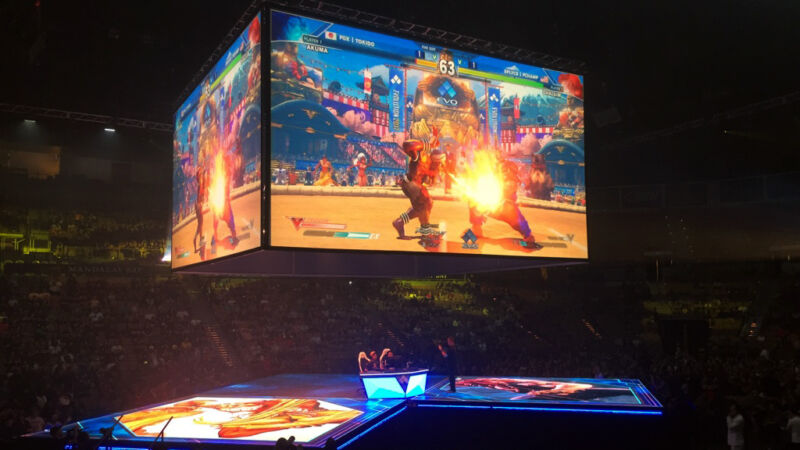 A video game plays on giant screens over a packed arena.