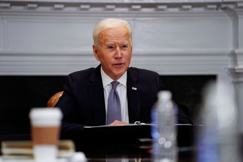 President Biden sitting at a table and speaking while gesturing with his hand.