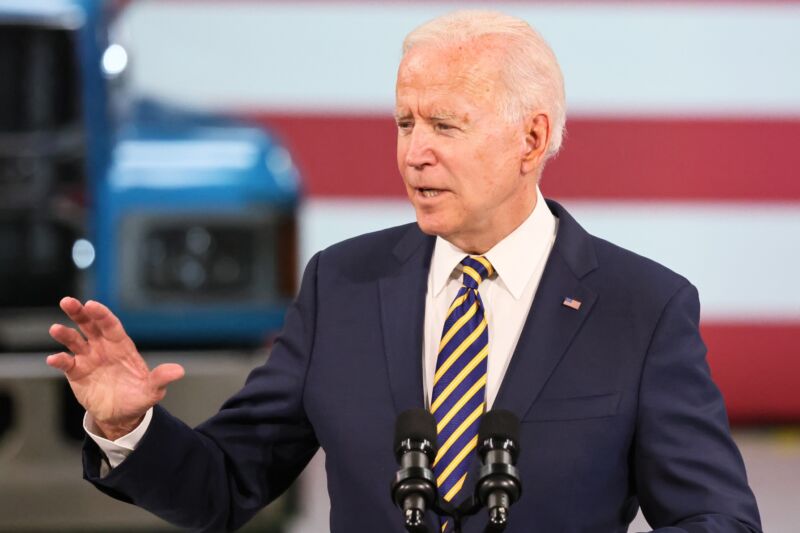 President Joe Biden speaking in front of a podium at a Mack Truck facility.