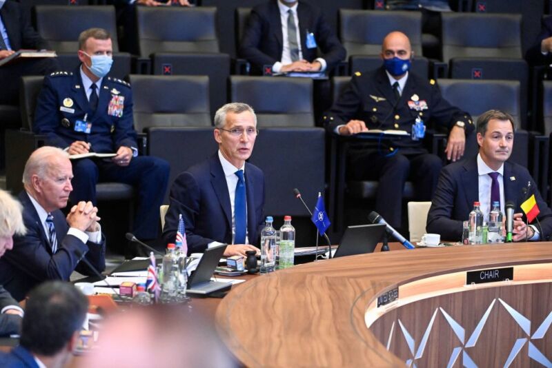 Men in suits and uniforms sit on one side of a long, curved table.