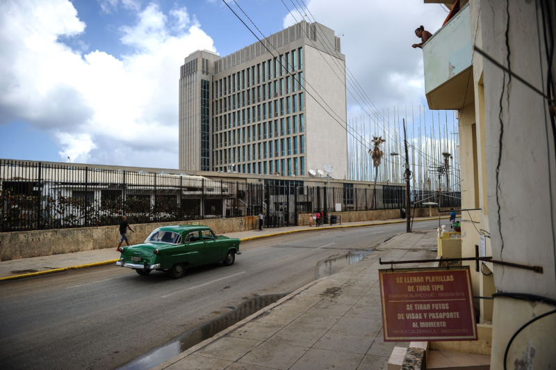 A beautifully maintained car from the '50s drives past a Brutalist skyscraper.