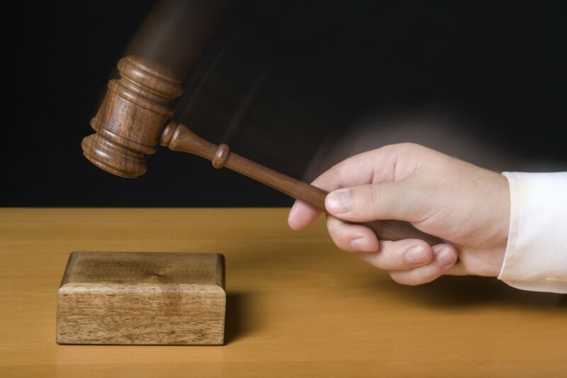 A judge's handing hitting a wooden block with a gavel.