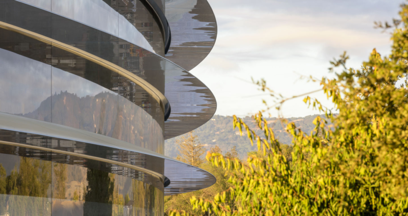 A tree-lined campus surrounds a multistory glass and steel building.