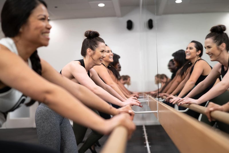 Pure Barre - Women laughing and doing a barre class.