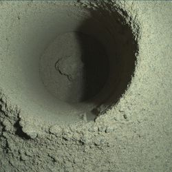 A closeup image of the borehole drilled by Perseverance, showing a mound of dusty material that scientists suspect slipped out of the rover’s drill bit tube.