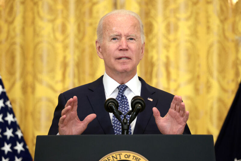 An older man in a suit speaks from a podium.