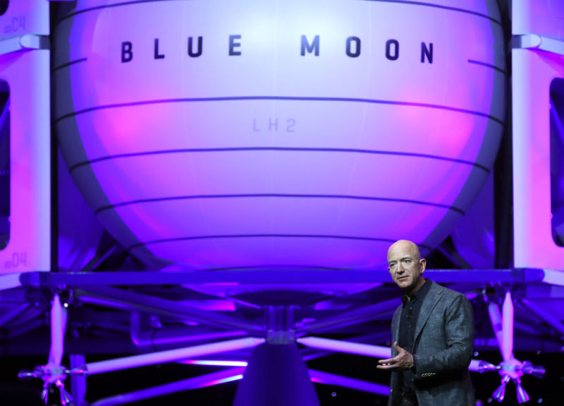 A man on a stage stands in front of full-size model of a spaceship.