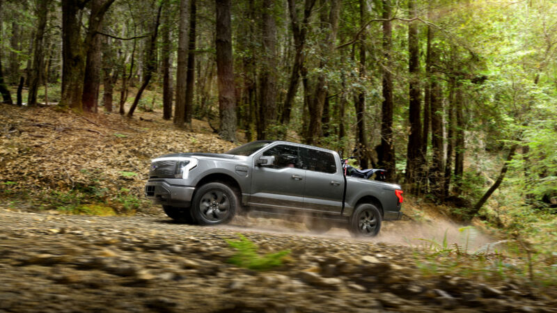 A Ford F-150 Lightning drives off road with a dirt bike in the back.