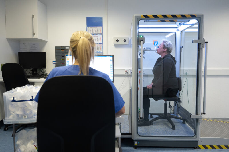 A woman breathes into a tube while a health care worker looks on.