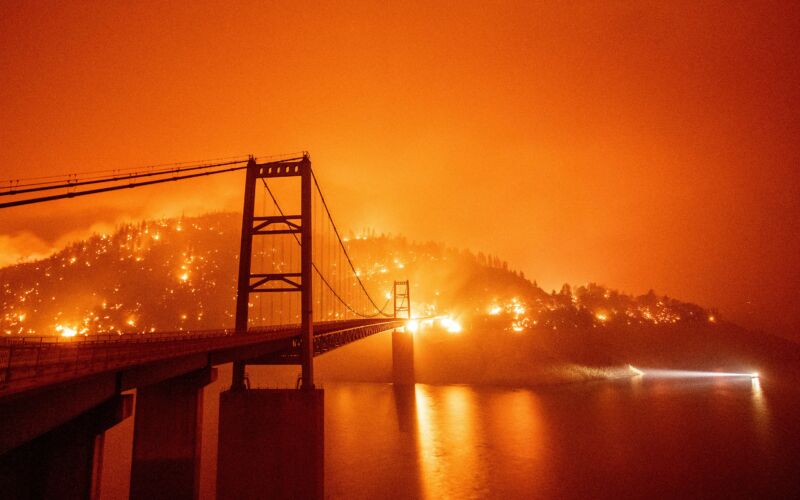 A deep orange sky covers an automobile bridge across a lake.