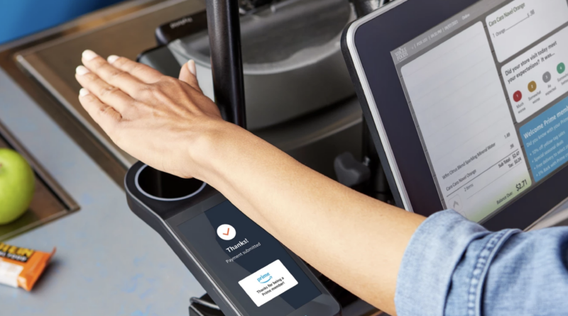 A customer uses a palm print reader in this promotional image for Amazon One.