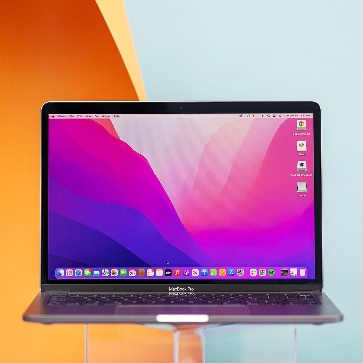 The MacBook Pro 13 2022 open on a transparent stand. The screen displays a pink and purple desktop background.