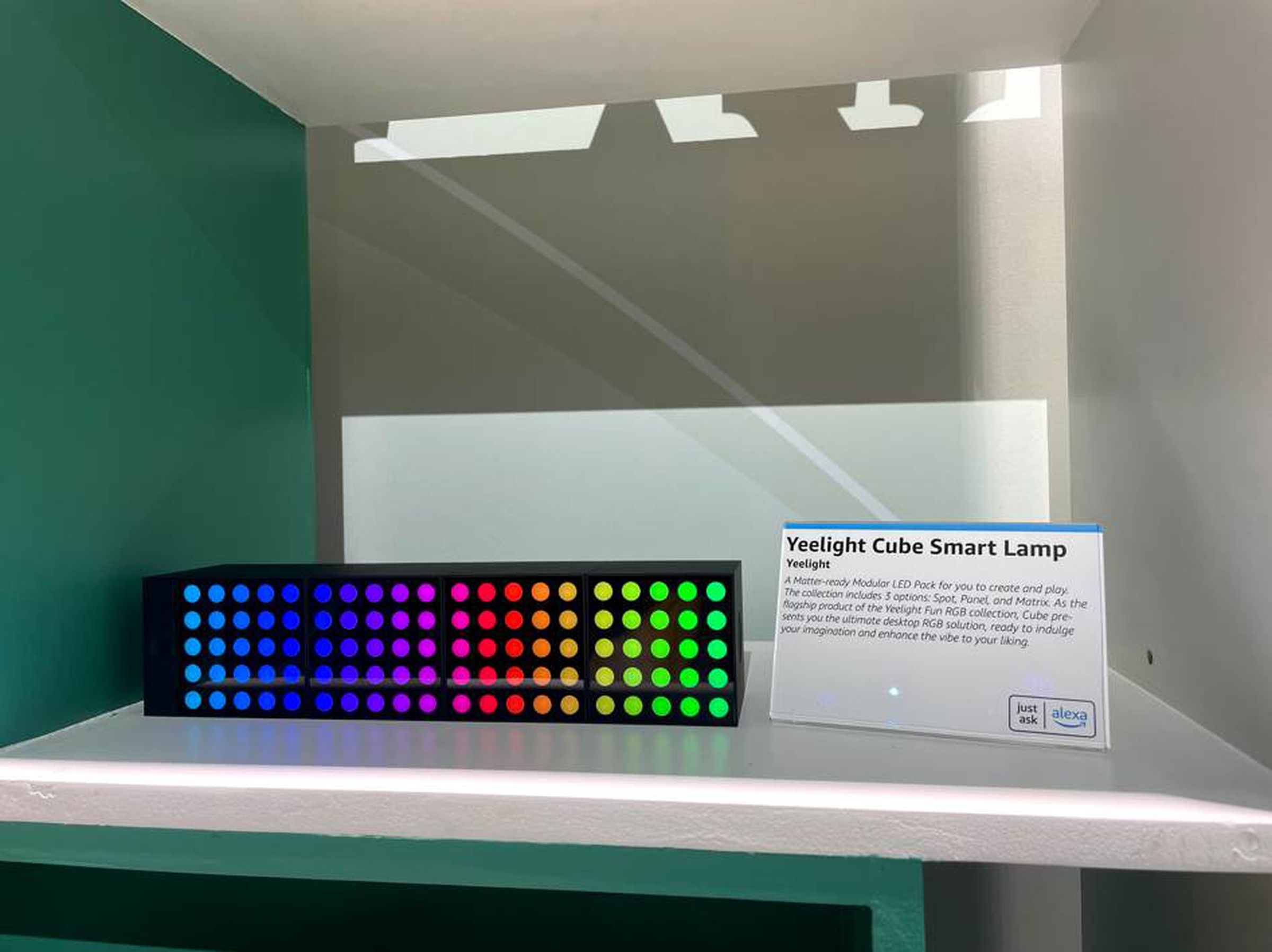 Four black cubes in a horizontal row. Each cube seems to have a 5x5 grid of circular LEDs on the front face. The LEDs are displaying a color gradient across all four cubes.