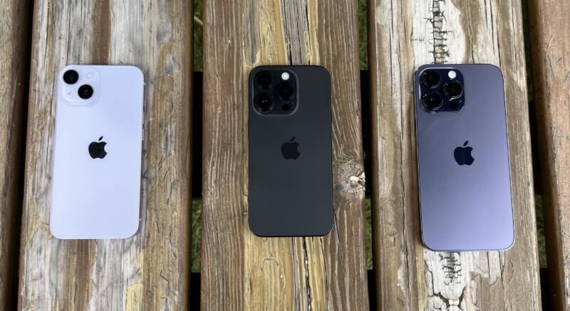 Three iPhones on a wooden picnic bench, with prominent cameras visible
