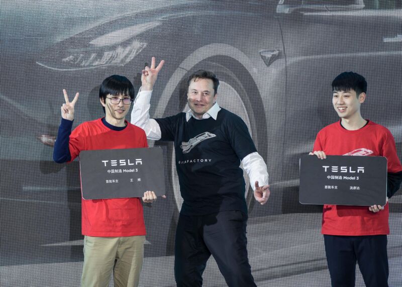 Elon Musk and a pair of Chinese fans wave on stage