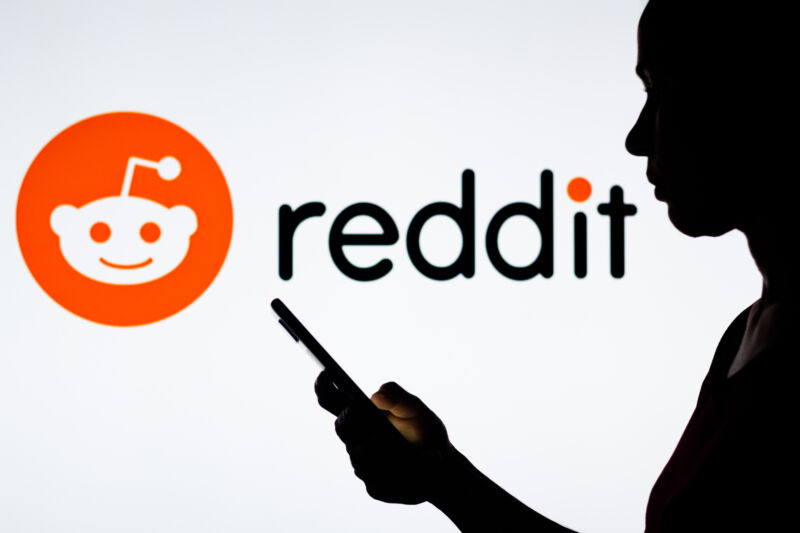 In this photo illustration, a woman's silhouette holds a smartphone with the Reddit logo in the background.