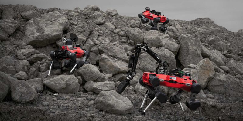 Image of three red, legged robots exploring rocky terrain.