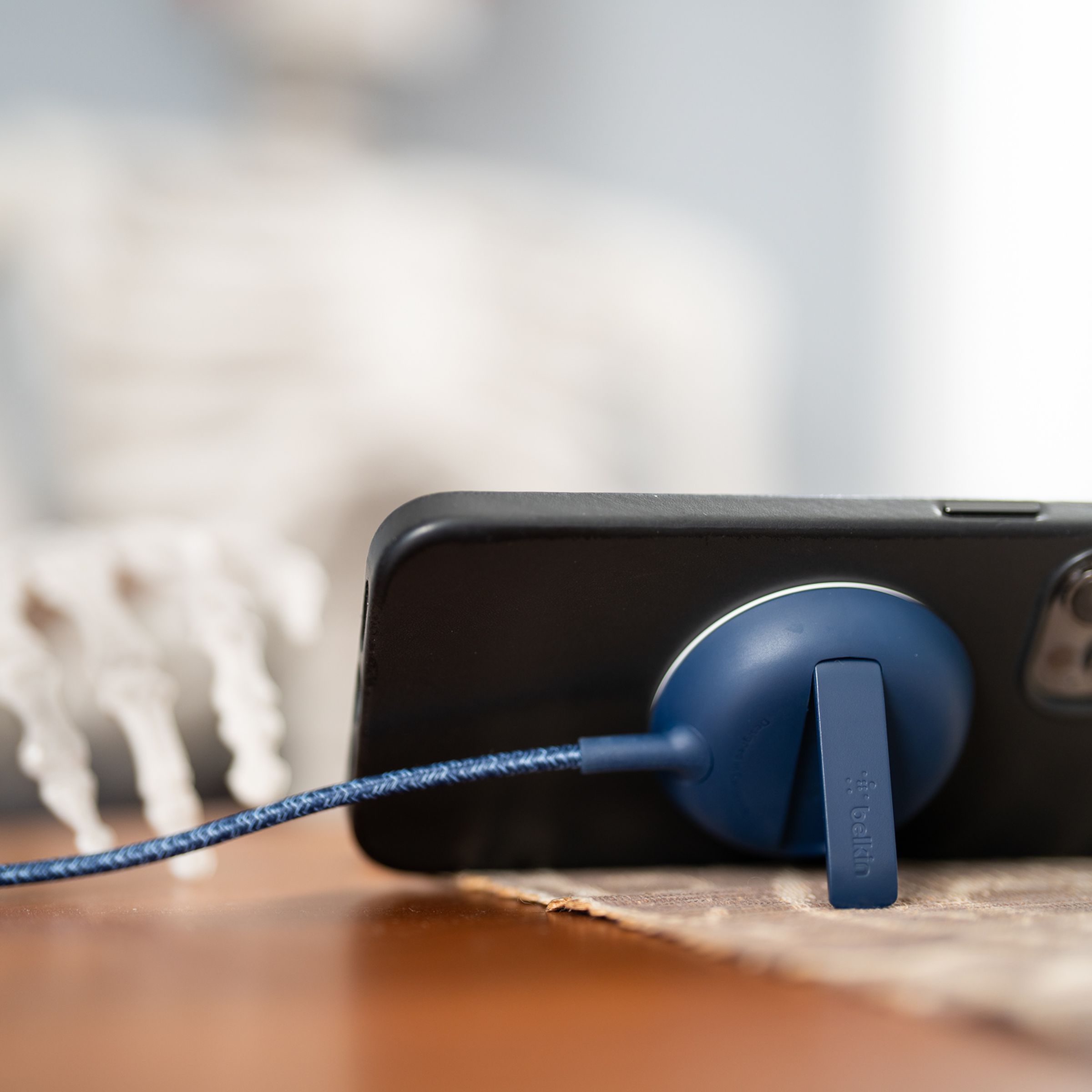 An iPhone propped up horizontally by the kickstand of a Belkin MagSafe charger on a table with a prop skeleton sitting in a chair and looking at the phone.