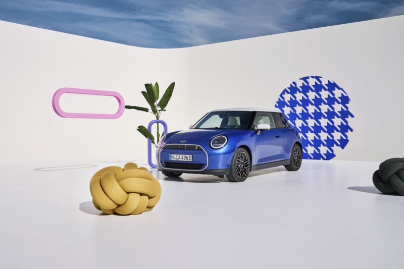 A blue mini Cooper with a giant knot next to it and patterns on some walls
