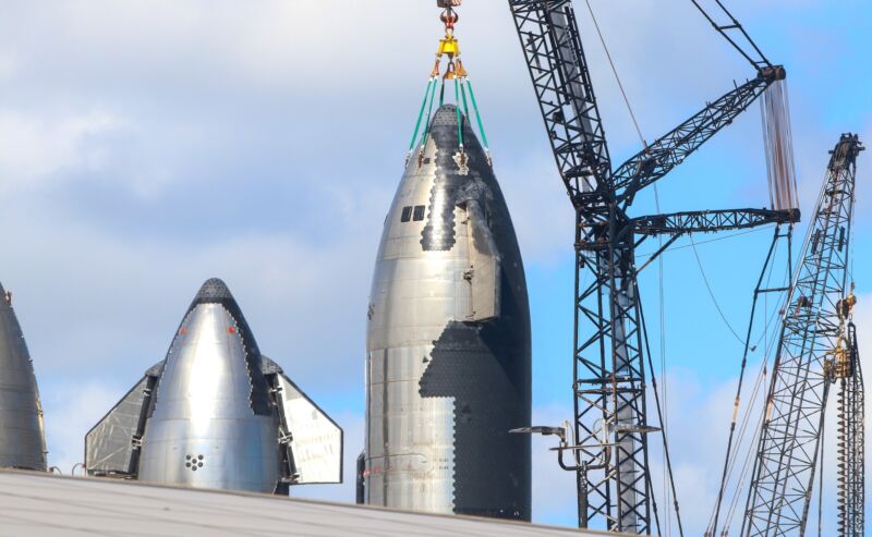 A crane is attached to one of several Starship test vehicles at SpaceX's Starbase facility in South Texas. This vehicle, called Ship 28, could launch on the next Starship test flight.