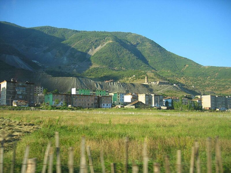 Image of apartment buildings with mine tailings behind them, and green hills behind those.