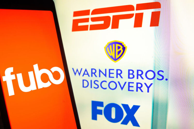 In this photo illustration, the FuboTV Inc. logo is displayed on a smartphone screen and ESPN, Warner Bros. Discovery and FOX logos in the background.