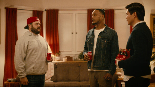 three men standing in a holiday home holding cans of coca-cola