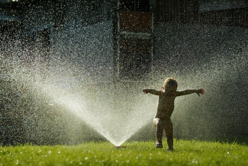 A child cools off under a water sprinkler.